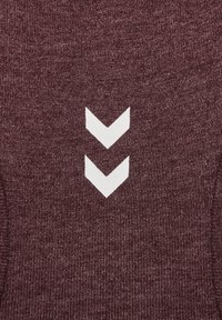 Bordeauxfarbener Strickstoff mit einem weißen Chevron-Muster. Die Textur ist glatt und hat einen leichten Stretch. Die Akzente sind subtil und gezielt.