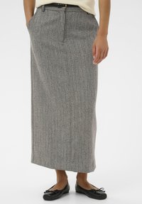 Jupe maxi en motif chevron gris en tissu texturé, dotée de poches latérales et d'une ceinture, associée à des ballerines noires.