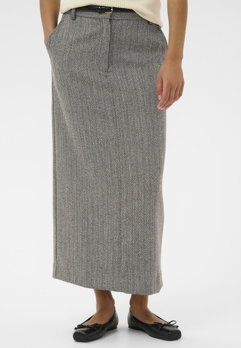 Jupe maxi en motif chevron gris en tissu texturé, dotée de poches latérales et d'une ceinture, associée à des ballerines noires.