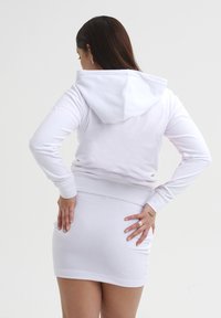 Felpa bianca con tasca a marsupio e polsini aderenti, abbinata a una mini gonna bianca coordinata. Tessuto liscio e design semplice.