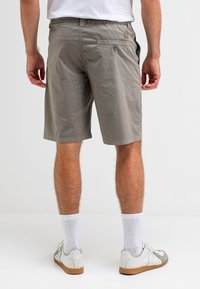Grijze katoenen shorts met een elastische tailleband, zijzakken en een knoopzak op de achterkant. Draagt witte sokken en casual schoenen.