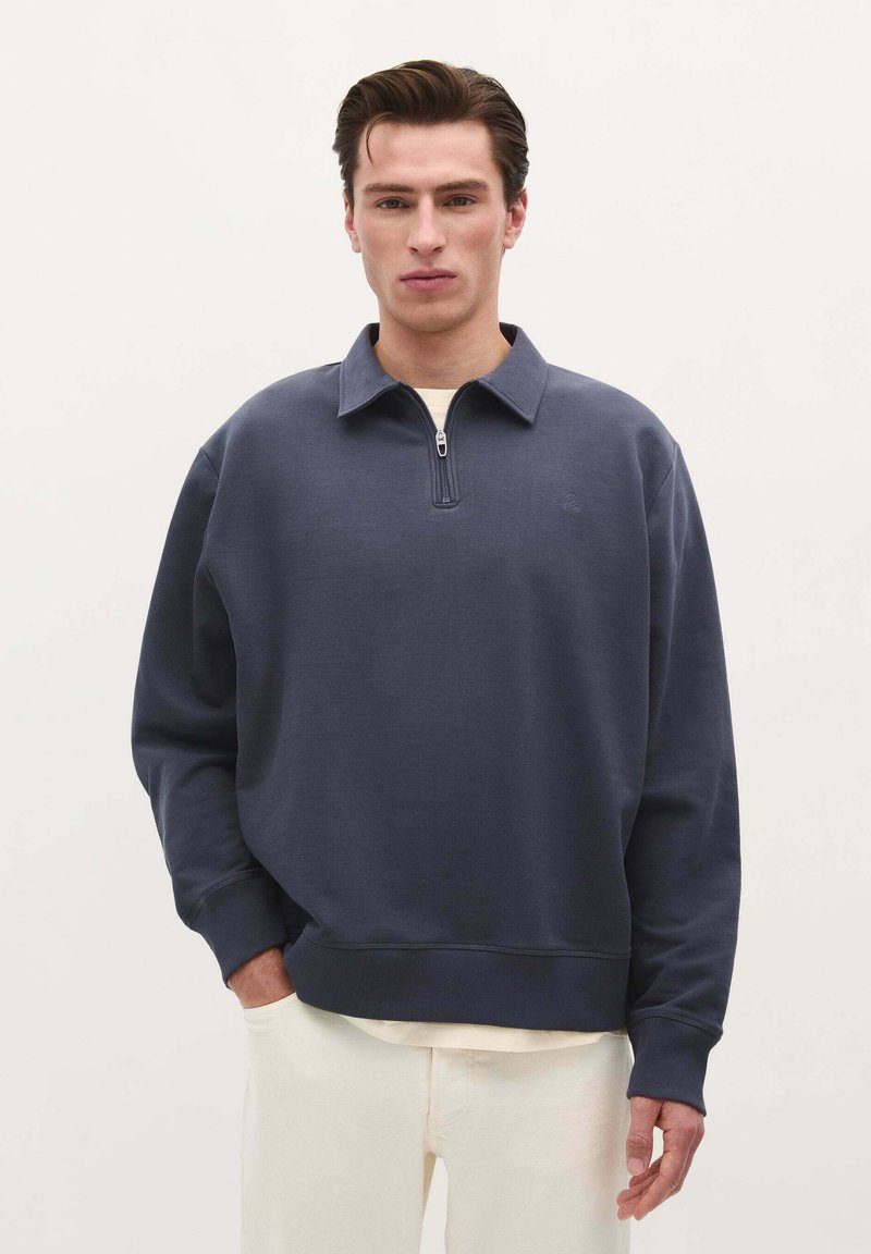 Marineblauwe sweatshirt met rits en een relaxte pasvorm, ribgebreide manchetten en een subtiele logodetail op de borst. Zachte stoftextuur.