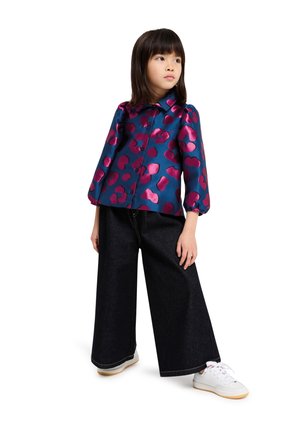 Blauwe satijnen blouse met bloemenprint en roze abstracte patronen, knoop aan de voorkant en pofmouwen, gecombineerd met wijde donkerdenim broeken en witte sneakers.