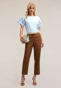 Lichtblauwe top met kantafwerking aan de mouwen, bruine tailored broek, gouden riem en een lichtblauwe en gouden handtas. Open teen, enkelband hakken.