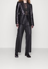 Blazer de cuero negro combinado con pantalones de pierna ancha a juego. La blusa transparente presenta un patrón floral. Botines de tacón bloque completan el look.