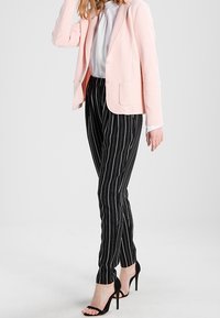 Světle růžový strukturovaný blazer přes bílou blůzu, doplněný černými pruhovanými kalhotami a černými sandály na vysokém podpatku.