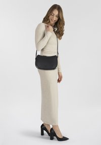 Bolso de hombro de cuero negro con un diseño curvo, cierre de cremallera y correa ajustable, llevado sobre un vestido ajustado de un beige claro.