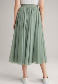 Mint-vihreä tüllimidi-hame, jossa on kerrottu vyötäröosa, pehmeä ja läpinäkyvä rakenne sekä kerroksellinen muotoilu, yhdistettynä valkoisiin tennareihin.