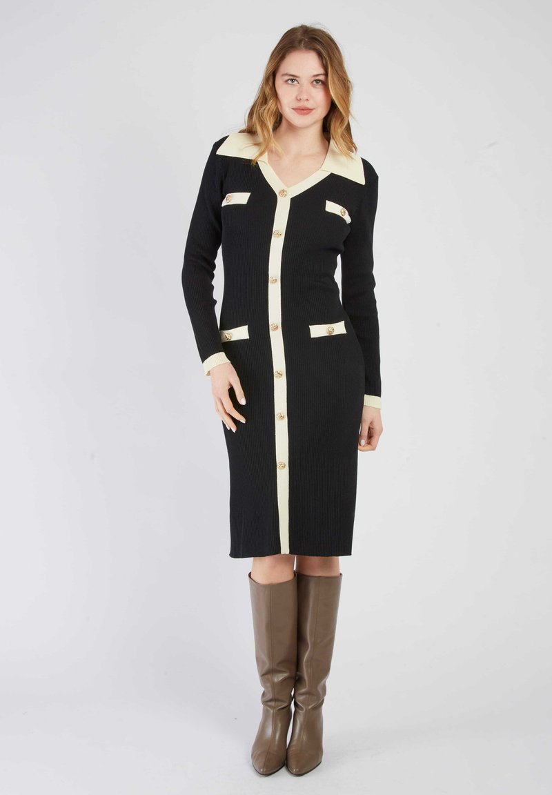 Czarna dzianinowa sukienka z kremowymi akcentami, dekoltem w serek, długimi rękawami, z zapięciem na guziki i przednimi kieszeniami. Nosi się ją z brązowymi, wysokimi na kolana botkami.