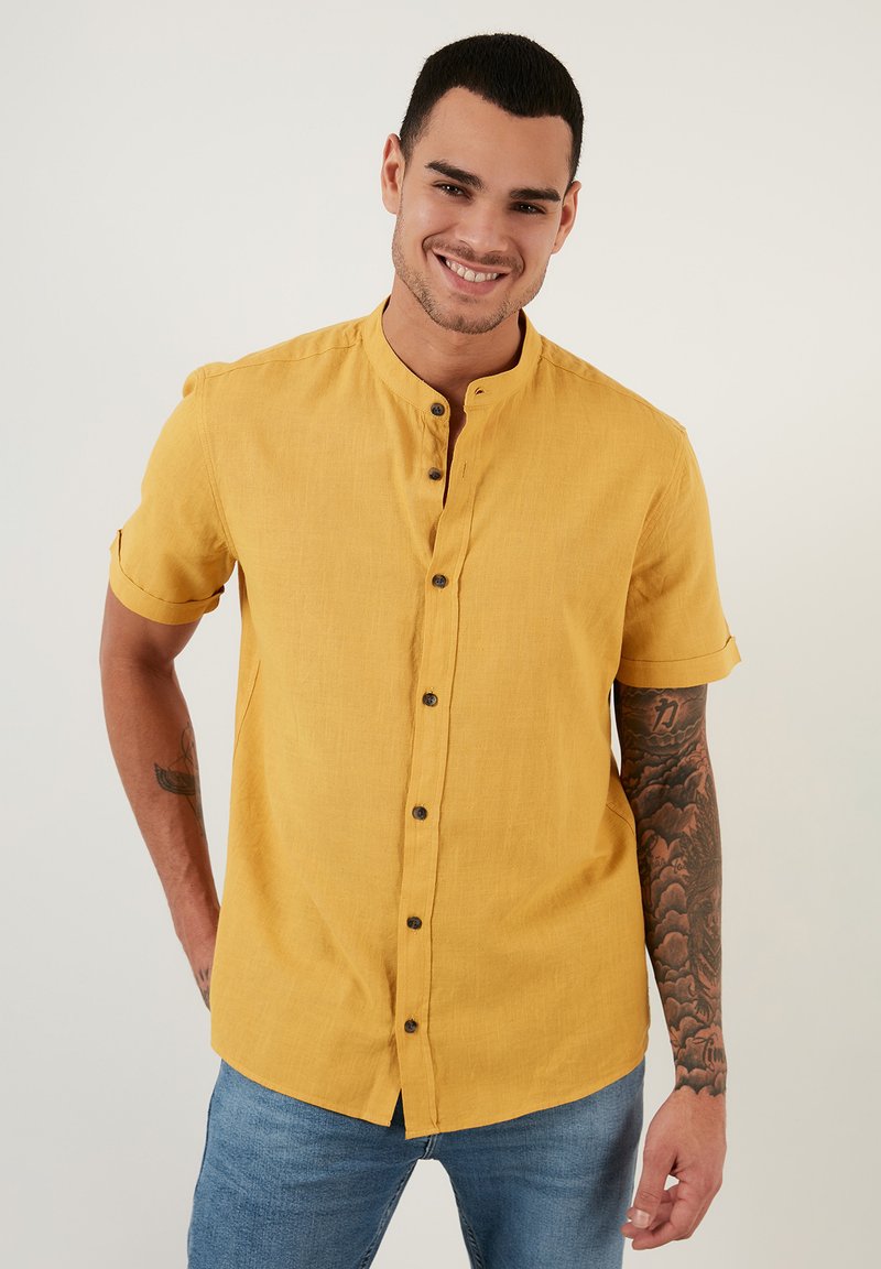 Camisa de manga corta, con botones, en lino amarillo brillante con cuello de tira, presenta botones marrones y puños enrollados.