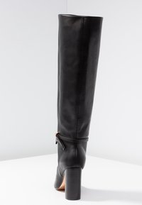 Black knee-high leather boot with a round toe, chunky heel, smooth texture, and a side zipper detail featuring a decorative accent.