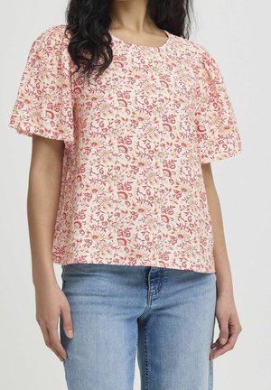 Vrouw draagt een roze bloemen korte mouwen blouse met opgepofte mouwen, gecombineerd met lichtblauwe jeans.