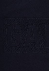 Marineblauwe sweatshirt met een getextureerd, pluche logo in donkerblauw, omgeven door een gladde stof rond het opvallende ontwerp.