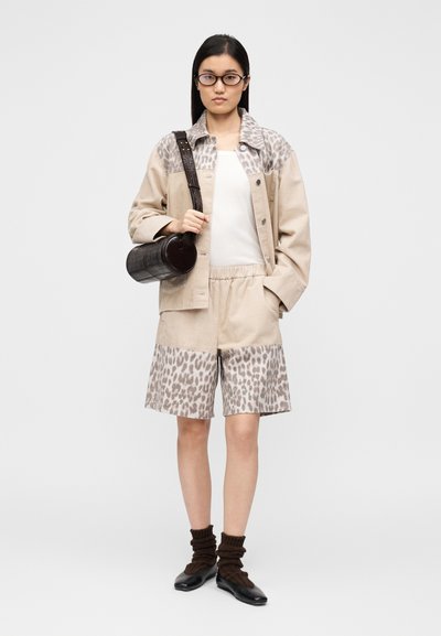 Μπεζ μπουφάν κορντό με λεπτομέρειες από λεοπάρ λεκέδες, λευκή μπλούζα, σορτς με σχέδια, καφέ κάλτσες και μαύρη στρογγυλή τσάντα.