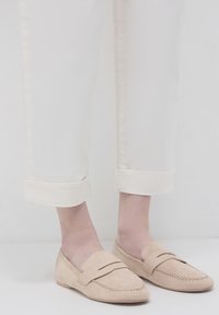 Beige Wildleder-Loafer mit einer genähten Naht und einem erhöhten Streifendetail über dem Rist. Kombiniert mit weißen, hochgekrempelten Hosen.