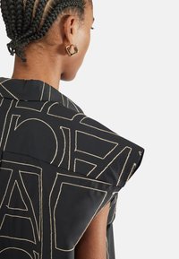 Maglietta senza maniche nera con audaci ricami geometrici dorati. Presenta un ampio colletto e spalle strutturate per una silhouette definita.