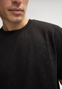 Schwarzes T-Shirt aus strukturiertem Stoff mit feinem Muster. Es hat einen Rundhalsausschnitt und kurze Ärmel und zeichnet sich durch eine figurbetonte Passform aus.