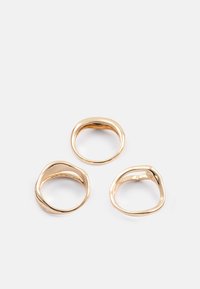 Tres anillos de oro con una forma suave y orgánica y un grosor variable. Tienen un acabado pulido y un diseño minimalista sin adornos.