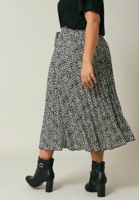 Zwart-witte luipaardprint midi-rok met plooien, gecombineerd met zwarte enkellaarsjes. Heeft een hoge taille en een vloeiende geur.