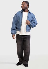 Világoskék, farmer anyagú bomber dzseki elasztikus mandzsettákkal és szegéllyel. Fehér póló fölött viselve, sötét, bő szárú farmerral párosítva.