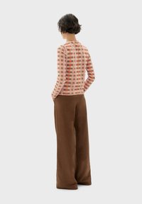 Sweater med et rosa og beige ternet mønster; parret med brune vide bukser; begge lavet af bløde materialer.
