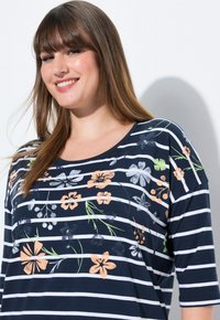 Top a righe blu navy con maniche corte, caratterizzato da stampe floreali in vari colori, tra cui pesca, bianco e verde. Texture del tessuto morbida.