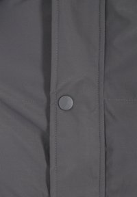 Szürke szövetkabát sima textúrával, lekerekített fekete patenttal és a varrások mentén látható cérnavarrással.