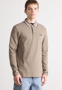 Polo de manga longa em algodão castanho claro com colarinho contrastante preto e branco, apresentando um pequeno logótipo preto no peito.