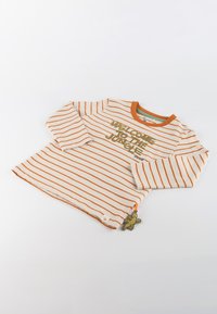Gestreiftes Langarmhemd in Creme mit orangefarbenen Streifen. Mit dem Text "WILLKOMMEN IM Dschungel". Dekorativer Eidechsen-Anhänger am Saum.