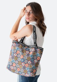 Bolso de tela estampado que presenta diseños geométricos multicolores, fabricado con un tejido que cuenta con una correa de logo audaz y en contraste, y un diseño espacioso.