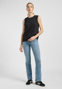 Sort ærmeløs top med rund hals, parret med lyseblå jeans og sorte sneakers med hvide striber. Enkel og casual design.