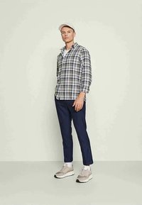 Rutet knappetrøye i grått og marineblått, sammen med marineblå bukser og lysegrå joggesko. Har lange ermer og en avslappet passform.