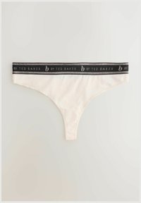 Krémové tangá s čiernym elastickým pásom s strieborným textom. Mäkký materiál, minimalistický dizajn a nízko strihaný štýl.