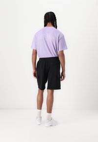 Fioletowa bawełniana koszulka z nadrukiem z tyłu i czarne szorty cargo. Białe sneakersy i skarpetki do kostek dopełniają strój. Minimalistyczny design.