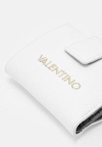 Portefeuille en cuir blanc texturé avec logo "Valentino" en ton doré, dotée d'une fermeture à rabat et d'un intérieur noir contrastant.
