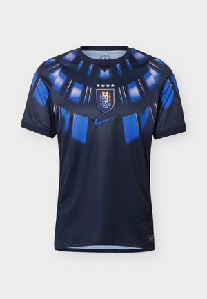 Ciemnoniebieska koszulka piłkarska z jasnoniebieskimi geometrycznymi wzorami, centralną tarczą herbową z literami A.U.F. i gwiazdami oraz niebieskim logo Nike pod tarczą.