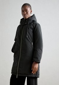 Black padded coat with a zip closure, adjustable hood, and side pockets. Features a smooth texture and slightly longer silhouette.