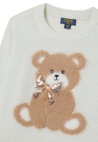 Hellbeiger, gestrickter Pullover mit einer strukturierten Applikation eines braunen Bären und einer Pailletten-Schleife. Der Stoff hat einen dezenten Glanz und eine weiche Oberfläche.