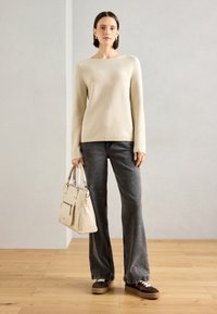 Suéter creme, jeans cinzentos flare, ténis castanhos e uma mala leve. Textura suave, design simples e palete de cores neutras.