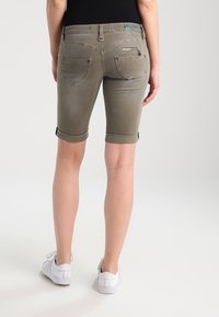 Shorts de mezclilla caqui con dobladillos enrollados, que cuentan con bolsillos traseros y un detalle de bolsillo con cremallera, estilizados con una cintura ajustada, llevados con zapatillas blancas.