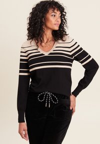 Schwarz-beige gestreifter Pullover mit langen Ärmeln und V-Ausschnitt, aus einem weichen Stoff gefertigt. Auffällige Details sind das strukturierte Strickmuster und die taillierten Ärmel.
