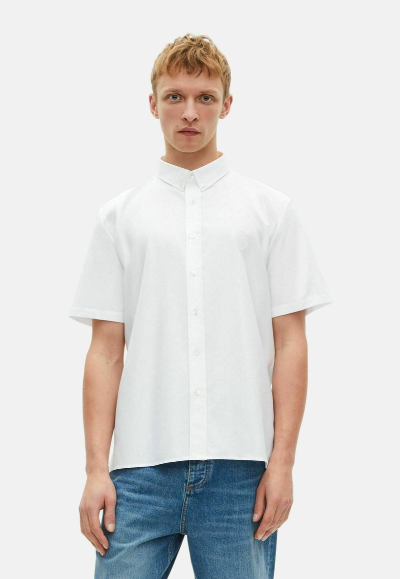 Witte shirt met korte mouwen en een kraag met knopen, voorzien van een subtiele geborduurde accenten, gecombineerd met blauwe denim jeans.