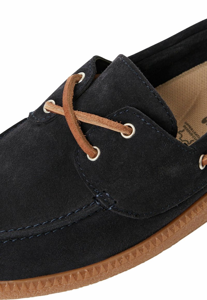 Ciemnoniebieski zamszowy but z brązowymi zamszowymi sznurówkami, metalowymi oczkami i teksturowaną gumową podeszwą z trójkątnymi wzorami.