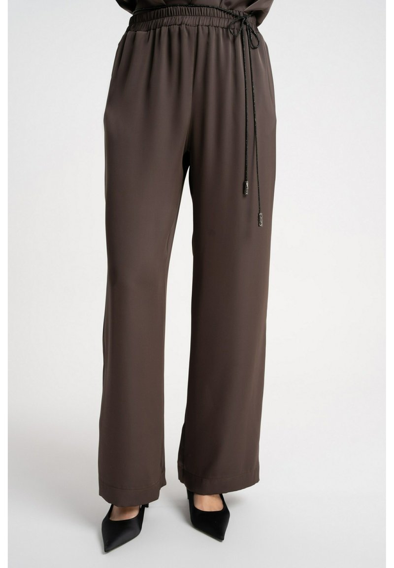 Brązowe spodnie o szerokich nogawkach wykonane z gładkiej tkaniny, z elastycznym pasem na gumce z troczkiem i czarnymi metalowymi akcentami. Dopasowane przy kostkach.