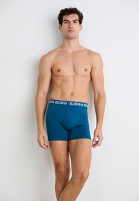 Boxer in teal con un elastico nero su cui è riportato il testo "BJÖRN BORG". Tessuto morbido, design aderente e lunghezza fino alla metà della coscia.