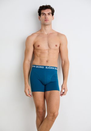 Tyrkysové boxerky s čiernym pásom s nápisom "BJÖRN BORG". Mäkká tkanina, priliehavý strih a dĺžka po stredný stehno.