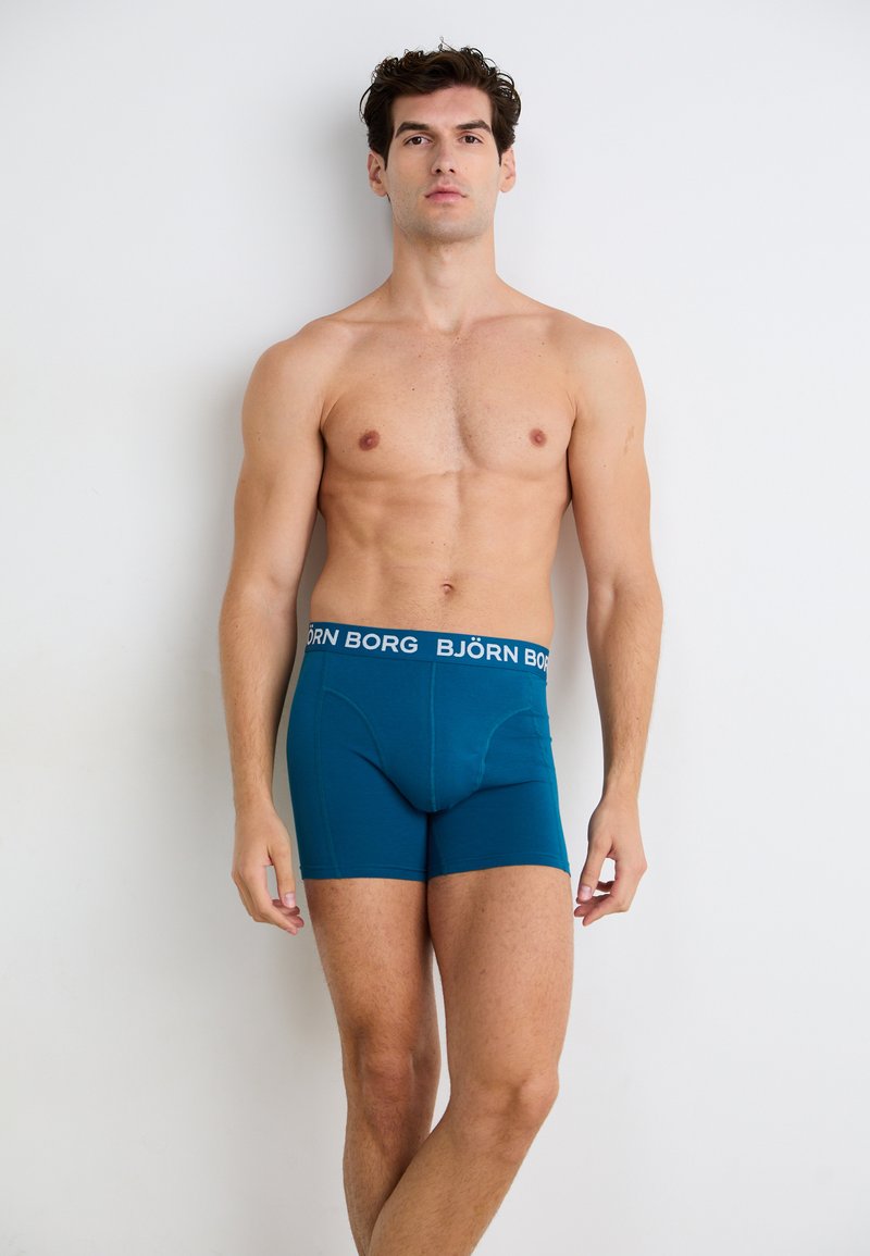 Boxer in teal con un elastico nero su cui è riportato il testo "BJÖRN BORG". Tessuto morbido, design aderente e lunghezza fino alla metà della coscia.