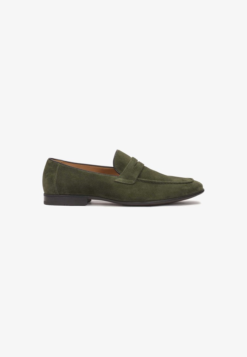Mocassins pour hommes en daim vert olive avec un petit talon noir et un détail de bride sur le dessus, vus de profil sur un fond blanc.