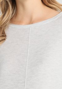 T-shirt grigia chiara realizzata in tessuto morbido, con scollatura rotonda e una leggera trama a coste, arricchita da un dettaglio di cucitura centrale.