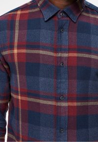 Rutig flanellskjorta i mörkblått, rött och tanfärgat. Har en spetsig krage, knappstängning och ett mjukt, texturerat tyg.